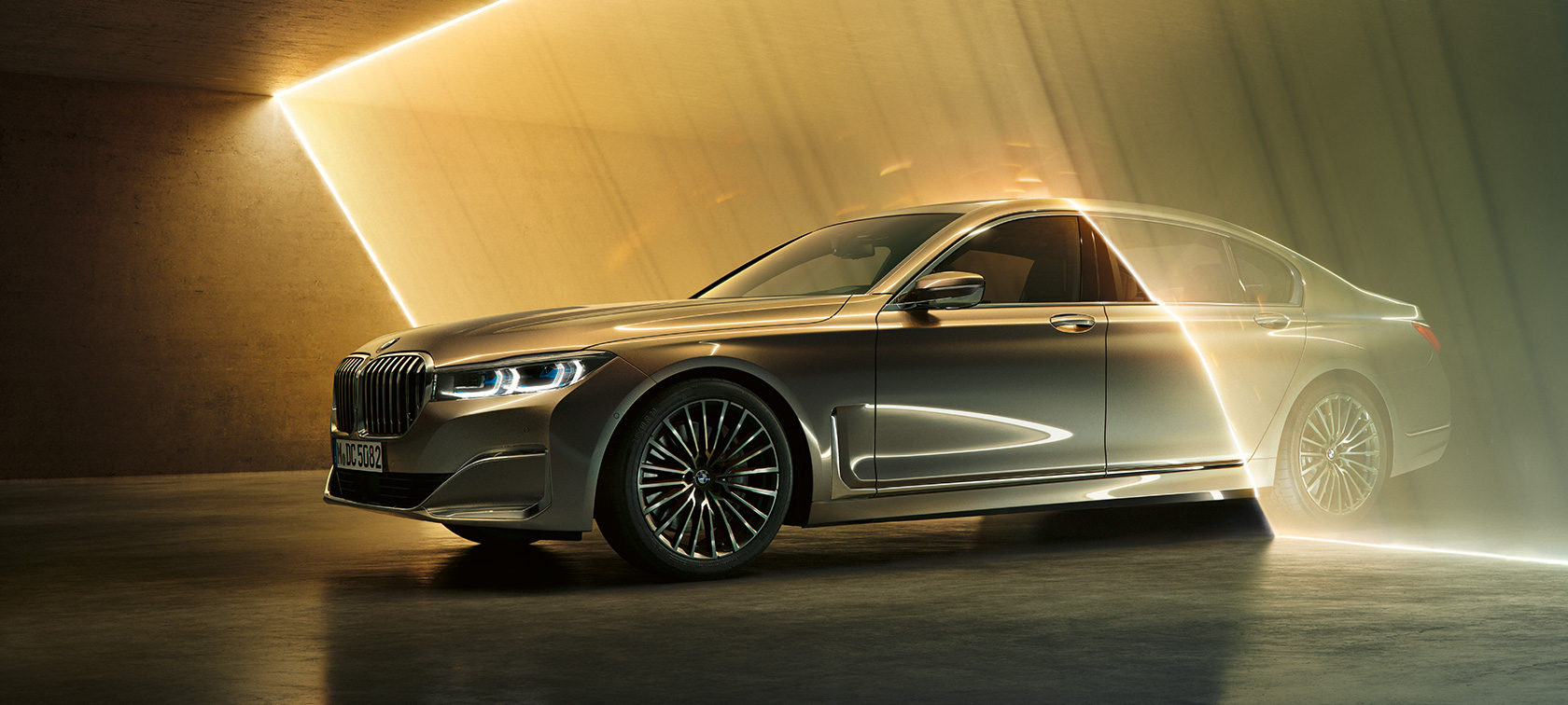 BMW Série 7 Berlina, perspetiva frontal a três quartos BMW Série 7 Berlina: perspetiva frontal a três quartos de um BMW em cinza rodeado por feixes de luz