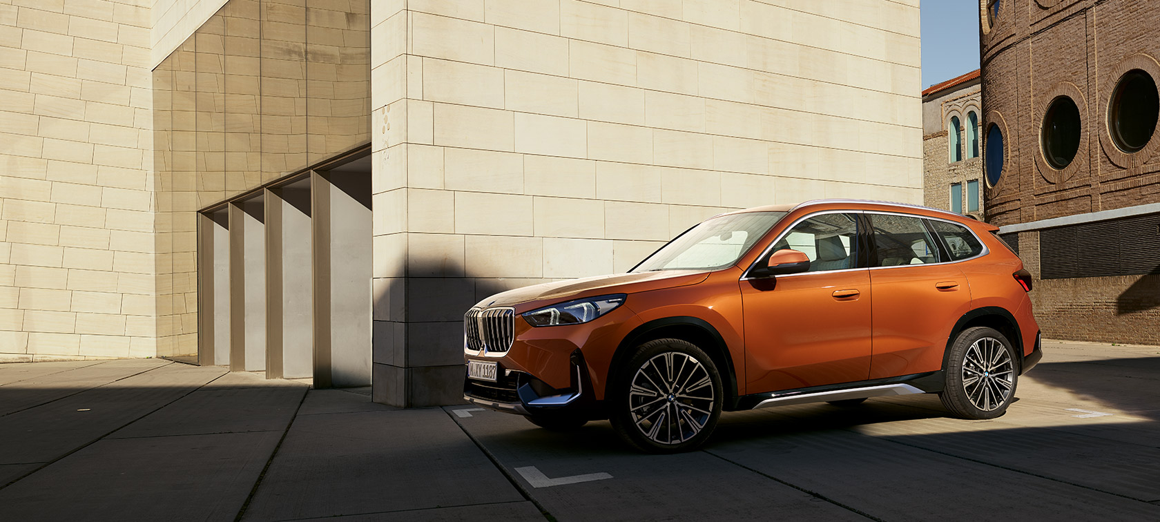 BMW U11, X1, Versão xLine, pintura laranja Utah metalizada, perspetiva dianteira a três quartos BMW U11, X1, Versão xLine, pintura laranja Utah metalizada, perspetiva dianteira a três quartos, parado à frente de um edifício